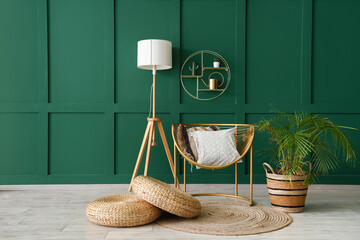 Stylish armchair with cushions, wicker poufs, lamp and houseplant near green wall