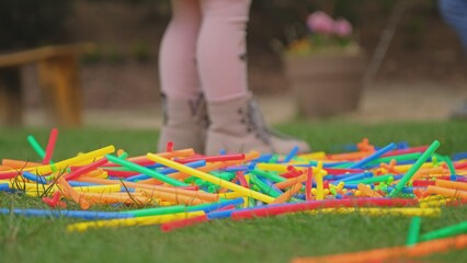 Cute Adorable Happy Caucasian Preschooler Girl Playing Outdoors with Colorful Construction Sticks Spread on Garden Grass Lawn	