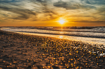 lowniczy zachód słońca nad morzem w miejscowości Sarbinowo. Promienie słońca malują wspaniałe odcienie złota na mokrym piasku plaży, tworząc magiczną atmosferę. 