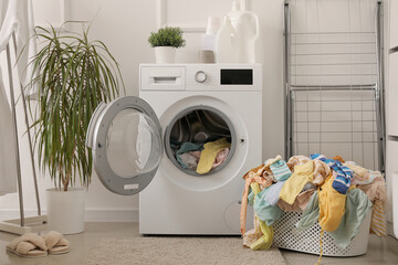 Basket with dirty clothes and washing machine in laundry room - obrazy, fototapety, plakaty