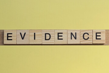 the word evidence of gray small wooden letters lies on a yellow table
