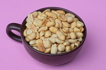gray brown peanuts in a ceramic cup on a pink table