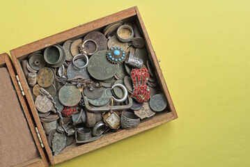 a pile of old coins of jewelry and ornaments in a wooden box on a yellow table