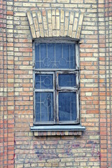 Fototapeta na wymiar one gray old wooden window with metal bars on the brown brick wall of the house on the street
