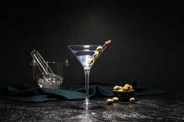 Glass of tasty martini with green olives and ice cubes on dark background