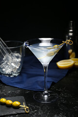 Glass of tasty martini, bucket with ice cubes and olives on dark background, closeup