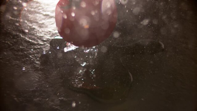 super slow motion of tomato falling into puddle of water