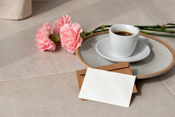 Blank paper card, postcard mockup, coffee cup, flowers on beige background in sun light, aesthetic holiday greeting or wedding design template