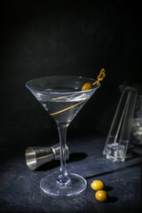 Glass of tasty martini and measure cup on dark background