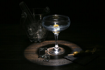 Glass of tasty martini, ice cubes and olives on dark wooden table