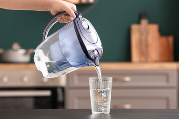 Woman pouring water from filter jug into glass on black table
