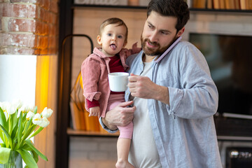 Father with little baby boy calling on smartphone at home and drinking coffee.