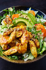Traditional German iceberg and Italian arugula salad served with chicken, avocado and vegetables with spicy sweet and sour curry sauce as a creative and flavorful meal on a plate