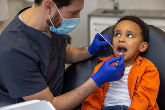 Dark-skinned boy looking scared while doctor checking up his teeth