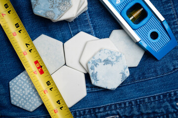 Collection of white hexagonal tiles next to measuring tape and a level on a denim background