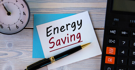 ENERGY SAVING - words on a white sheet on the background of a calculator, alarm clock and pen