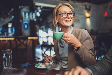 one mature caucasian blonde woman have a cup of coffee sit at cafe