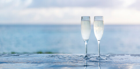 Two glasses of champagne on the side of the infinity pool against the backdrop of a sunset in the Maldives. Banner