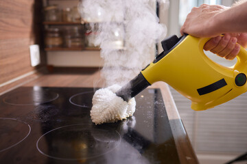 Cleaning kitchen hob with a steam cleaner.
