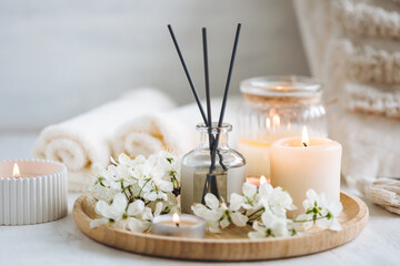 Obraz na płótnie Canvas Aroma diffuser, burning candle, cherry blooming flowers and perfume on wooden bamboo tray. Cozy home decor, hygge and aromatherapy concept. Comfortable atmosphere, spring delicious fresh smell
