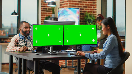 Asian digital editor looking at greenscreen on multiple monitors, working with chroma key display in agency studio. Female employee using blank mockup template and isolated copyspace.