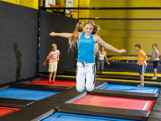 Full length of cheerful teenage girl in sportswear having fun while jumping high on colorful trampoline at game club