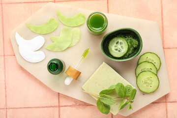 Board with cotton under-eye patches, mint and cucumber slices on beige tile background