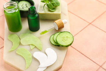 Board with cotton under-eye patches and cucumber slices on beige tile background, closeup