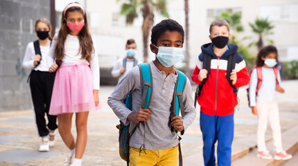 African american tween schoolboy in protective mask with backpacks going to school lessons on fall...