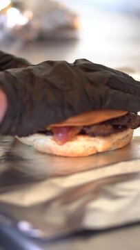 Preparing cheddar cheese and bacon burgers with black gloves on fast food restaurant