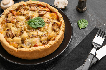 Mushroom pie with spinach leaves and cutlery on black grunge table