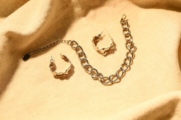 Fototapeta na wymiar Beautiful chain bracelet and earrings on color fabric background