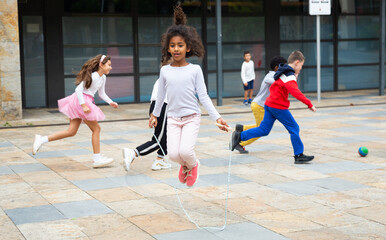 Happy schoolgirl jumping game by rubber band, kids friends on background