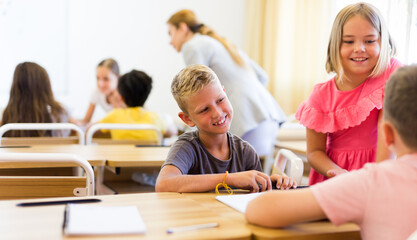 Fototapeta premium Schoolchildren performing group tasks in classroom. Teacher standing beside and observing.