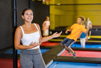 Fototapeta na wymiar Portrait of cheerful young female in sportswear posing and smiling at camera on colorful trampoline at game club