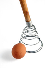 Beige chicken egg and spiral whisk. Ingredients for cooking isolated on white background