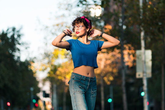 bella mujer adolescente estilo 80s 90s andando en skate en la ciudad, con maquillaje, anteojos y jeans. en un día soleado al atardecer.