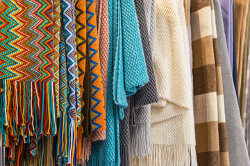 Close-up of multi-colored plaids, stoles hanging in store, cozy seasonal goods. Autumn winter...