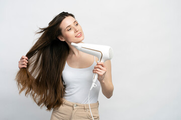 Naklejka premium Beautiful young woman with long silky straight hair looking aside using hair dryer