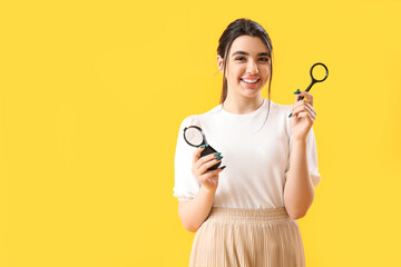 Young woman with magnifiers on yellow background