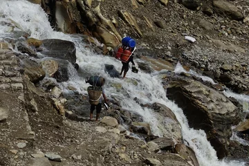 Cercles muraux Manaslu Resilient local porters conquer icy currents, carrying heavy goods across the Manaslu Glaciers in the Nepalese Himalayas, showcasing unwavering teamwork amidst nature's challenges.