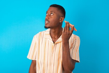 Smiling young man wearing fashion shirt over blue background listening a voice message from her...