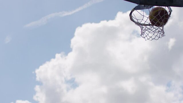 Slight variation of basketball going through the net in slow motion on an outdoor court