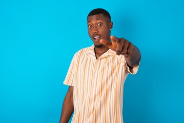 Excited positive Handsome man wearing fashion shirt over blue background points index finger directly at you, sees something very funny. Wow, amazing