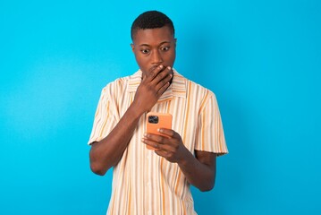 Handsome man wearing fashion shirt over blue background being deeply surprised, stares at...