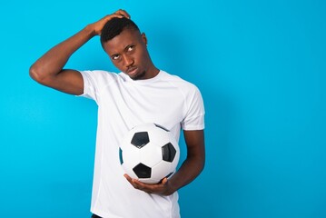 Young man wearing white T-shirt holding a ball over blue background saying: Oops, what did I do?...