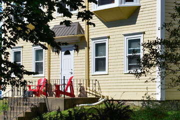 The exterior of a vintage yellow colored wooden clapboard country style house with red Adirondack...