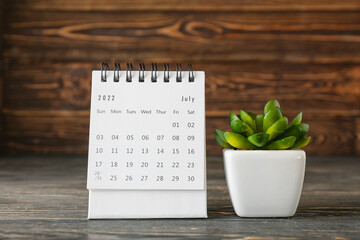 Fototapeta na wymiar Flip paper calendar for July and houseplant on table, closeup