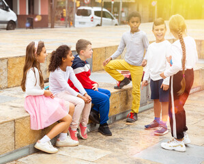 Group of smiling children sitting on stairs and chatting together sitting at urban street