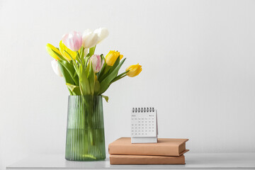 Flip paper calendar, notebooks and vase with flowers on table